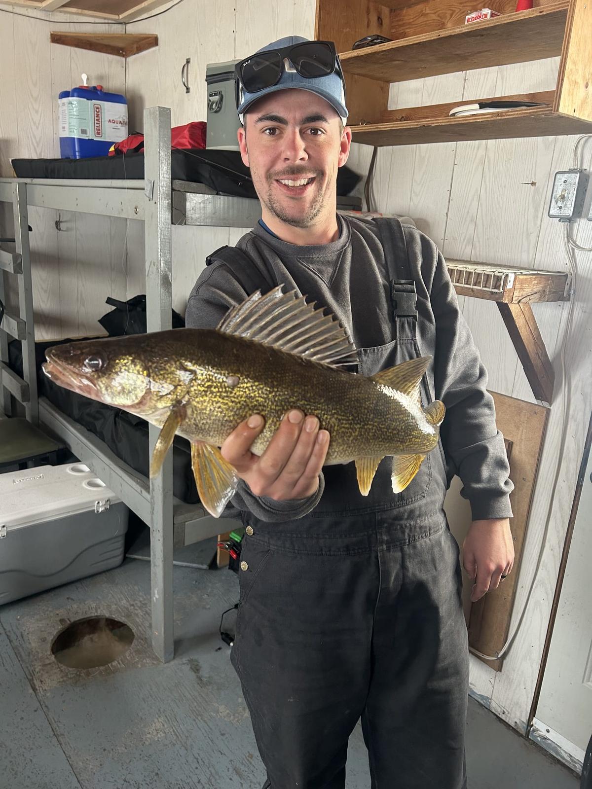 Troy Giesler holding a walleye inside a Lakeside Ice Condos ice fishing hut on Lake Nipissing